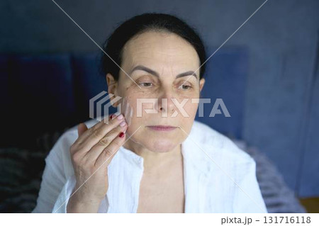 a senior woman in underwear on the bed performs routine self-care with face and body cosmetics, face foam a senior woman in underwear on the bed performs routine self-care with face and body cosmetics, face foam 131716118
