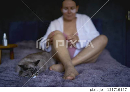 a senior woman in underwear on the bed performs routine self-care with body cosmetics 131716127