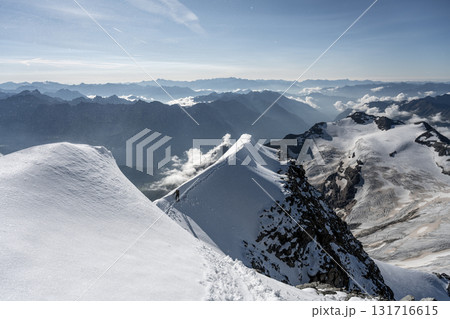 Adventurers navigate the sharp, steep exposed ridge of Piz Palu in the Bernina range during summer, surrounded by stunning alpine scenery and glistening snow. 131716615