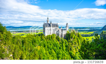Neuschwanstein Castle rises dramatically above lush green forests and rolling hills in Bavaria, Germany. Neuschwanstein Castle rises dramatically above lush green forests and rolling hills in Bavaria, Germany. 131716639