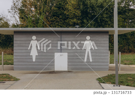 Public restroom building with male and female symbols on a wooden facade. Outdoor sanitation facility, accessible toilet at rest area 131716733