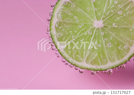 A fresh lime slice rests against a pink background, featuring tiny bubbles clinging to its surface. The vibrant green color of the lime stands out, creating a refreshing look. A fresh lime slice rests against a pink background, featuring tiny bubbles clinging to its surface. The vibrant green color of the lime stands out, creating a refreshing look. 131717027