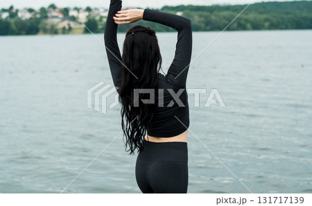 A young woman in dark sportswear is practicing gymnastics on the beach 131717139
