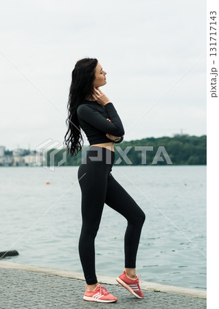 A girl with an athletic build poses by the lake in black leggings and a tight-fitting shirt 131717143