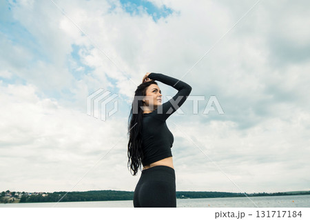 A woman with long dark hair in black leggings stands by clear water 131717184