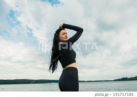 An athlete with an athletic build poses in black clothing against the backdrop of a natural landscape 131717185