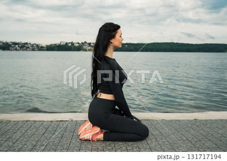A woman with a slender athletic build performs gymnastics exercises against the backdrop of a lake A woman with a slender athletic build performs gymnastics exercises against the backdrop of a lake 131717194
