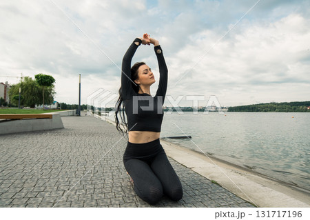 A woman with a slender athletic build performs gymnastics exercises against the backdrop of a lake 131717196