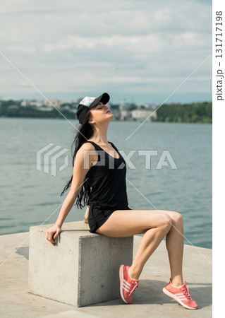 A young girl with an athletic build sits on the shore of a lake, enjoying the silence A young girl with an athletic build sits on the shore of a lake, enjoying the silence 131717198