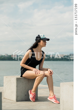 A young girl with an athletic build sits on the shore of a lake, enjoying the silence A young girl with an athletic build sits on the shore of a lake, enjoying the silence 131717199