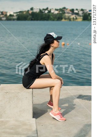 An athlete with a toned figure is sitting by the clear water 131717207