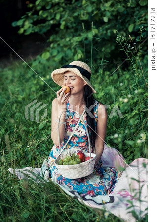 A girl at a picnic wearing a hat and a floral dress 131717218