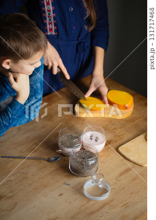 Brother watching sister slice fresh mango for chia pudding 131717468