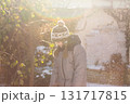 Happy boy in knitted winter hat playing outside under falling snow in sunlight 131717815