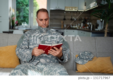 Soldier reading a book sitting on the sofa at home 131717967