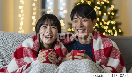暖炉の前でブランケットに包まり、恋人たちがホットココアを飲みながら寄り添っている 131718286