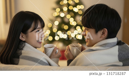 暖炉の前でブランケットに包まり、恋人たちがホットココアを飲みながら寄り添っている 131718287