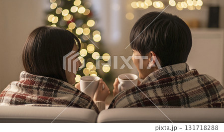 暖炉の前でブランケットに包まり、恋人たちがホットココアを飲みながら寄り添っている 131718288