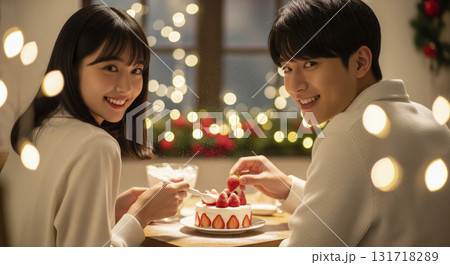 恋人たちが小さなクリスマスケーキを一緒に作っている。女性がクリームを塗り、男性が苺をのせる。 131718289