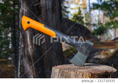 Tourist ax on a stump in a summer forest. Chopping wood with an ax. Tourist camping. Summer day. The concept of adventure and freedom. 131718335