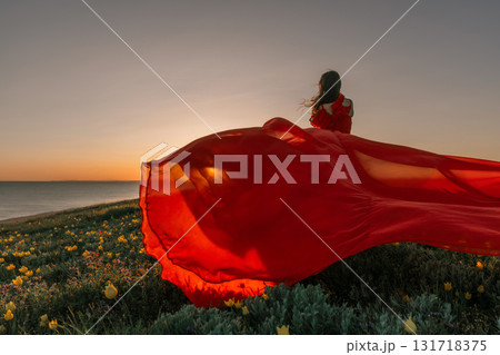 Dress Sunset Woman: Woman in red dress gazes at sunset by sea, enjoying freedom, on grass field. 131718375