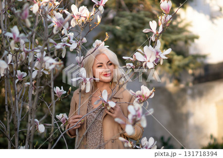 A woman is holding a magnolia flower in her hand and standing in front of a tree. Concept of serenity and beauty, as the woman is surrounded by nature and the flower adds a touch of color. 131718394