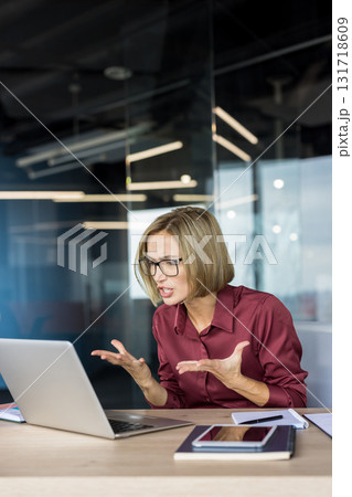 Businesswoman with short hair and glasses looks upset and stressed, gesturing and arguing during a tense video call on her laptop in a modern office workplace, remote meeting conflict Businesswoman with short hair and glasses looks upset and stressed, gesturing and arguing during a tense video call on her laptop in a modern office workplace, remote meeting conflict 131718609