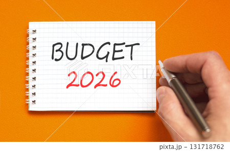 Budget 2026 symbol. Concept words Budget 2026 on beautiful white note. Beautiful orange paper background. Businessman's hand with pen. Business and budget 2026 concept. Copy space. 131718762