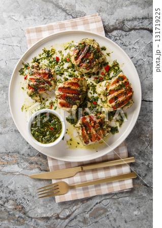 Grilled chicken thighs marinated and drizzled with chimichurri sauce, close-up on a plate. Vertical top view Grilled chicken thighs marinated and drizzled with chimichurri sauce, close-up on a plate. Vertical top view 131719225