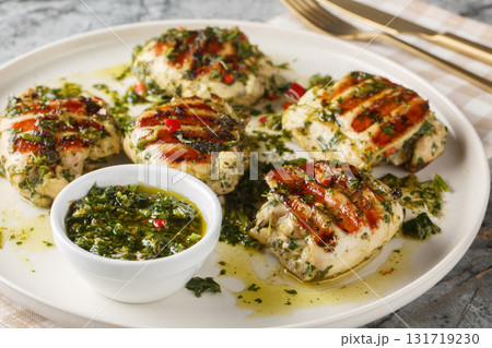 Grilled chimichurri chicken thighs with garlic, herbs and vegetable oil close-up in a plate. Horizontal Grilled chimichurri chicken thighs with garlic, herbs and vegetable oil close-up in a plate. Horizontal 131719230