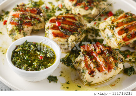 Grilled chicken thighs marinated and drizzled with chimichurri sauce, close-up on a plate. Horizontal Grilled chicken thighs marinated and drizzled with chimichurri sauce, close-up on a plate. Horizontal 131719233