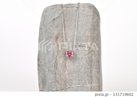 A pink heart pendant is displayed on a rock 131719602