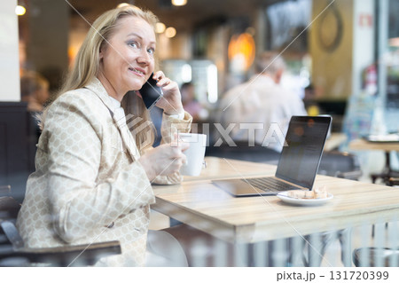 Businesswoman sitting at cafe table and talking on mobile phone Businesswoman sitting at cafe table and talking on mobile phone 131720399