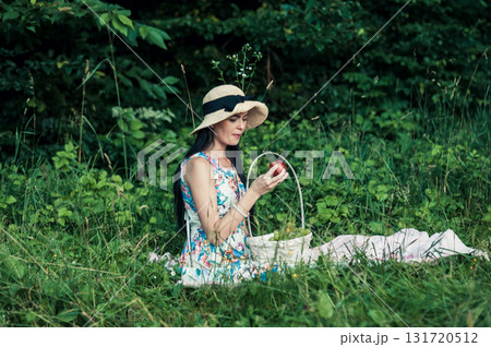 A beautiful girl at a picnic wearing a cute hat is holding a red nectarine 131720512