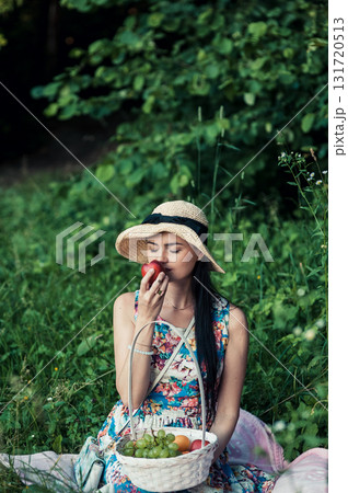A beautiful girl at a picnic wearing a cute hat is holding a red nectarine 131720513