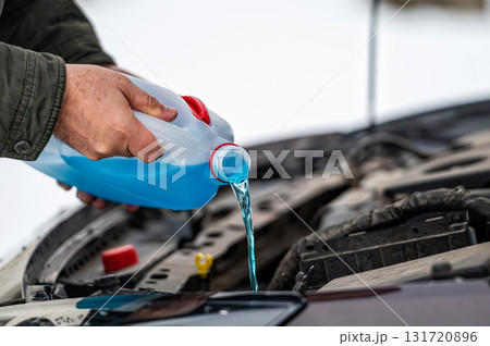driver refilling the blue non-freezing windshield washer liquid in the tank of the car, close-up driver refilling the blue non-freezing windshield washer liquid in the tank of the car, close-up 131720896