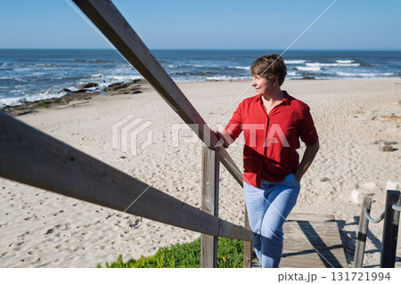 Middle-aged woman sitting on a wall looking at the ocean in Portugal, enjoying a sunny summer day 131721994