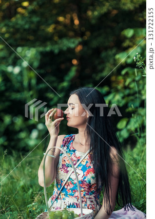 A woman in a bright floral dress sits on a soft pink rug at a picnic A woman in a bright floral dress sits on a soft pink rug at a picnic 131722155