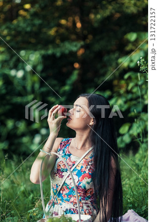 A woman in a bright floral dress sits on a soft pink rug at a picnic A woman in a bright floral dress sits on a soft pink rug at a picnic 131722157