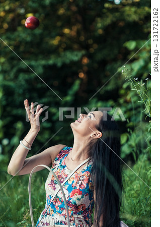 A seductive girl in a floral dress sits on a pink rug at a picnic 131722162