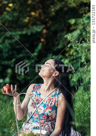 A lady in a light floral dress sits on a pink rug surrounded by nature 131722165