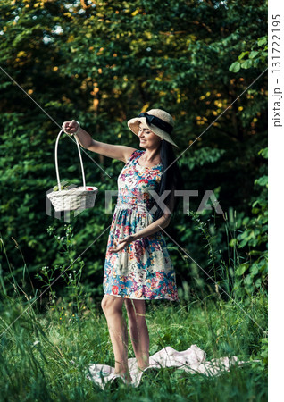 A woman at a picnic stands among the greenery near a pink rug 131722195