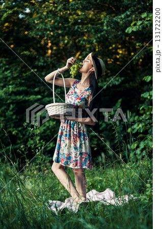 A young girl stands on green grass next to a pink picnic blanket 131722200