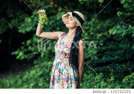 A young girl stands on the grass with a bunch of green grapes 131722225