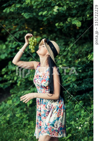 A woman in a floral dress holds a bunch of grapes A woman in a floral dress holds a bunch of grapes 131722229