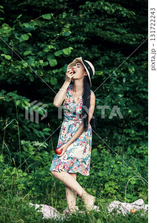 A young girl stands in the green forest with two red apples A young girl stands in the green forest with two red apples 131722243