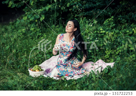 A lady in a cute dress sitting with a cup of tea among the greenery of the park 131722253