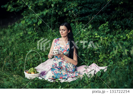 A lady in a cute dress sitting with a cup of tea among the greenery of the park 131722254