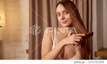 Woman brushing long smooth hair with calm expression at home Woman brushing long smooth hair with calm expression at home 131722265