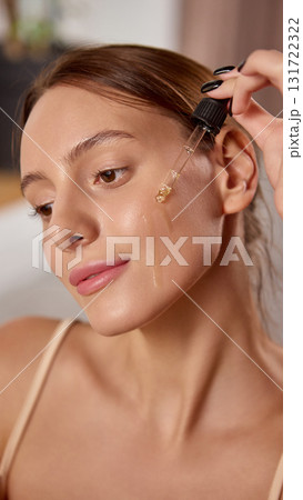 Woman applying face serum with dropper for skincare hydration and radiance 131722322